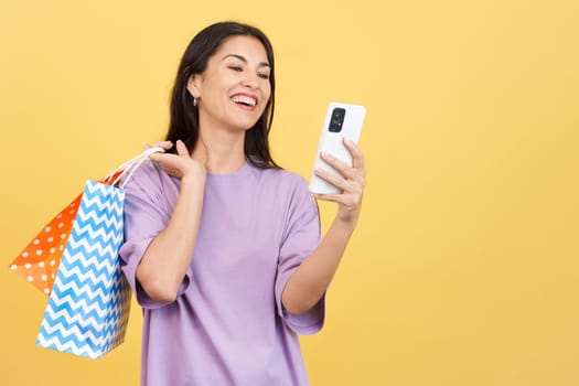 Happy caucasian woman using the mobile while holing shopping bags