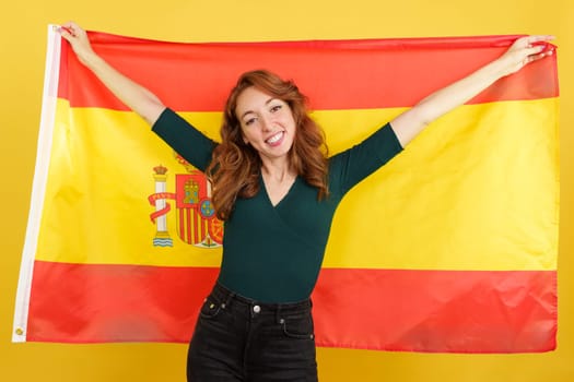 Happy redheaded woman smiling and raising a spanish national flag
