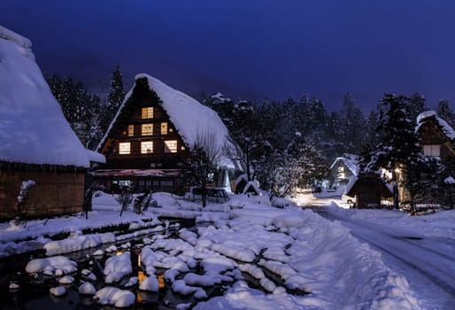 Snow covered Japanese farmhouse in historic village by woods at night