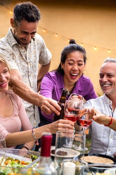 Vertical portrait of asian young woman toasting with wine, celebrating with friends, laughing. Garden dinner party.