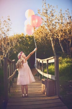 Balloons make me happy. a happy little girl holding balloons and a teddy bear while standing in the middle of a bridge.