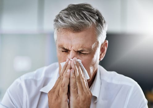 These allergies are getting to me. a mature businessman blowing his nose in the office.