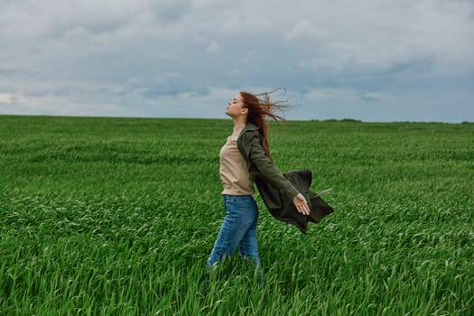 a woman in a coat stands in the middle of a field in cloudy weather in a strong wind turned sideways to the camera. High quality photo