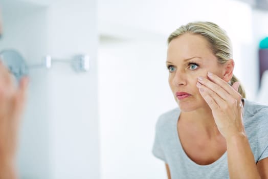 Analysing her skin for any blemishes. a mature woman inspecting her skin in front of the bathroom mirror.