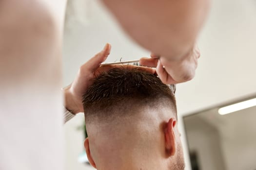 hairdresser does haircut for man using comb and grooming scissors