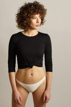 Slim woman in underwear standing against gray backdrop