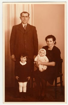 Vintage photo shows family in the photography studio. Retro black and white photography with sepia effect.