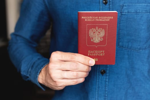 Russian foreign passport in the right hand of a man in a blue denim shirt