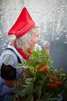 Girl in black school uniform, white apron and red tie near fountain water with bouquet of flowers. Nostalgia photo shoot of teenager of female pioneer from USSR costume for September 1 or graduation