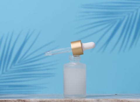 White glass dropper bottle with cosmetic product on a blue background