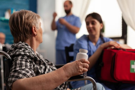 Retired woman in wheelchair holding pills talking to nurse