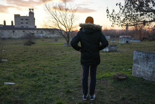 Slender tall man standing looking at an abandoned building in winter sunset