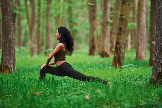 Positive brunette doing fitness outdoors in the forest at daytime