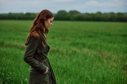 a beautiful, red-haired girl in a raincoat stands in a field in the spring in rainy weather. High quality photo