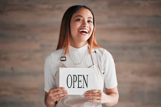 Cafe, portrait and woman holding an open sign in studio on a blurred background. Coffee shop, small business startup and management with a young female entrepreneur indoor to display advertising