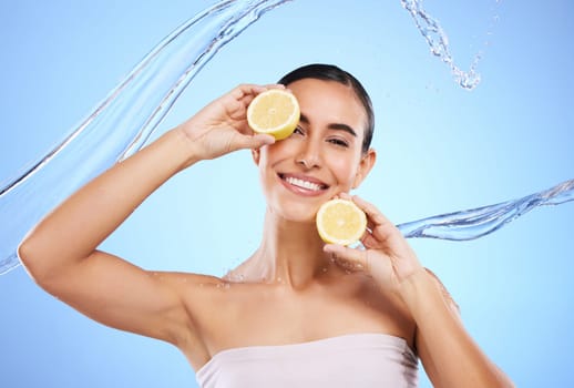 Vitamin c, lemon and water splash with portrait of woman in studio for natural cosmetics, nutrition and detox. Glow, fruits and hydration with female on blue background for diet, face and skincare