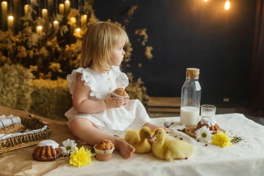 A little girl is sitting on the Easter table and playing with cute fluffy ducklings. The concept of celebrating happy Easter.