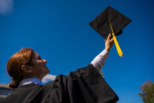 A woman throws her graduation cap against the blue sky.