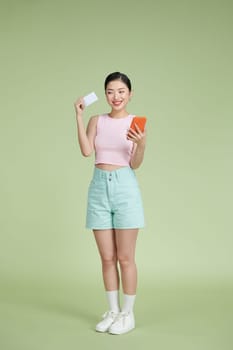 Young asian woman isolated on green background buying with the mobile with a credit card