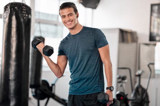 Portrait, dumbbells and man in gym smile with earphones for streaming music while exercising. Sports workout, fitness and happy bodybuilder or athlete lifting weights for exercise, health and muscle.