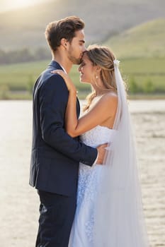 Love, wedding and a couple kissing by a lake outdoor in celebration of marriage for romance as newlyweds. Water, summer or kiss with a bride and groom bonding together in tradition after ceremony.
