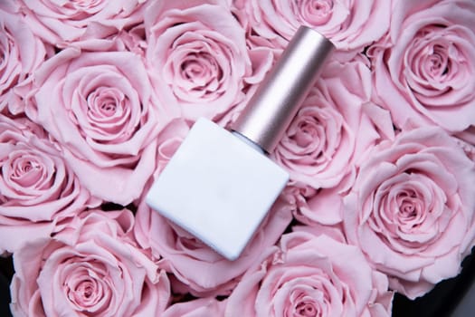 Nail polish bottle with white mockup for text lies on pink roses, background,