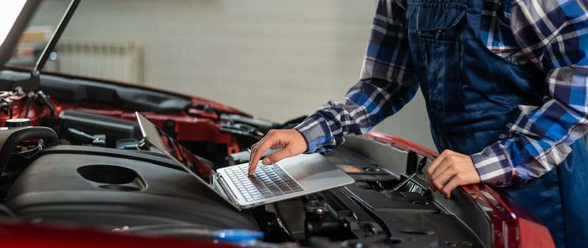 Woman auto mechanic doing engine diagnostics using laptop.