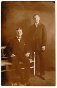 Vintage photo shows young boys brothers pose in a photography studio. Retro black and white photography with sepia effect. Circa 1910s.