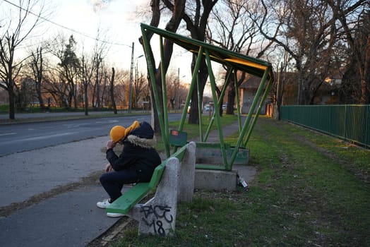 Young man sitting at a bus stop sad holding his head