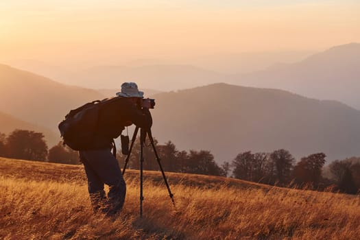 Male photographer standing and working at majestic landscape of autumn trees and mountains by the horizon.