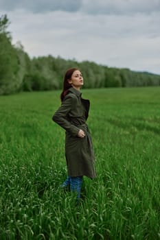 a beautiful woman in a dark coat stands in a green field in the spring in rainy weather