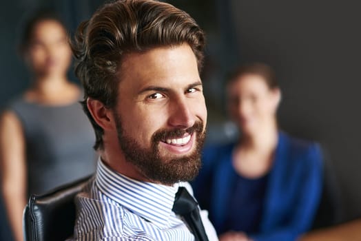 Success has put a smile on his face. Portrait of a smiling businessman sitting in an office with colleagues in the background.