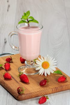 Glass of milk shake with mint and fresh strawberries on a wooden board