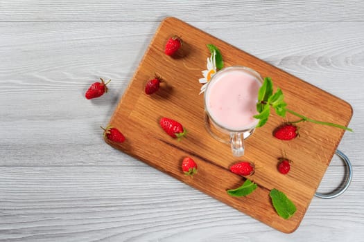 Glass of milk shake with mint and fresh strawberries on a wooden board