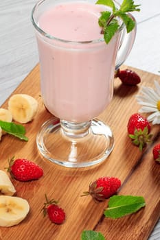 Glass of milk shake with mint and fresh strawberries, banana on wooden board