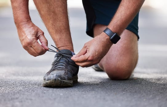 Hands, shoes and running with a senior man tying his laces outdoor on a road during a cardio workout. Fitness, exercise or footwear with a male runner getting ready for endurance training on a street