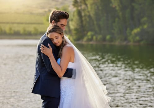 Wedding couple, hug and relax by lake for love on romantic getaway or honeymoon in nature. Calm woman hugging man in happy marriage relaxing by the water together enjoying the loving embrace outdoors