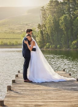 Wedding couple, hug and relax by lake for honeymoon, love or romantic getaway in nature. Calm woman hugging man in happy marriage relaxing by the water together enjoying the loving embrace outdoors