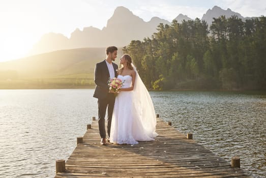 Love, married or romance with a bride and groom on a pier over a forest lake in nature after their ceremony. Wedding, love and water with a young couple in celebration of their marriage outdoor.