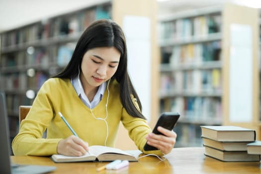 Student studying at library using phone.