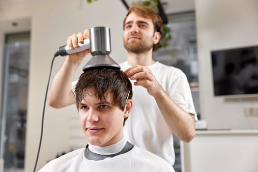 Professional hairdresser during work with man client with hair dryer