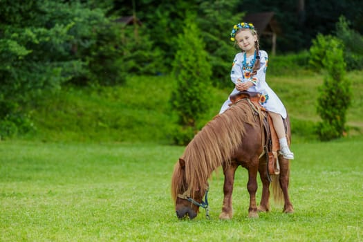 Little girl in Ukrainian national costume rides a pony