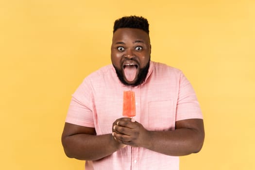 Bearded man holding pink cold ice cream and showing tongue out, feels hungry.