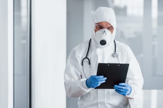 Male doctor scientist in lab coat, defensive eyewear and mask holding notepad in hands