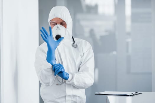 Male doctor scientist in lab coat, defensive eyewear and mask wearing blue gloves