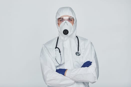 Male doctor scientist in lab coat, defensive eyewear and mask standing against white background