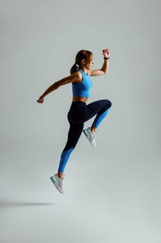 Sporty determined woman running in Mid-Air exercising during cardio workout over studio background