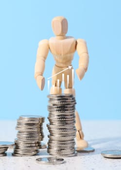 Wooden mannequin and a stack of coins on a blue background. Business indicators growth concept, income growth