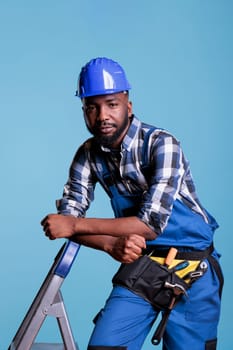 Builder looking calm leaning against ladder in studio shot