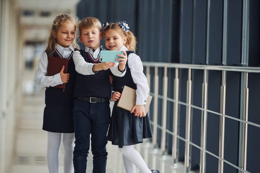 School kids in uniform together with phone and making selfie in corridor. Conception of education